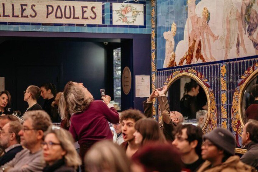 A crowded indoor venue with a blue tiled wall and a sign reading 'ALLES POULES.' 5