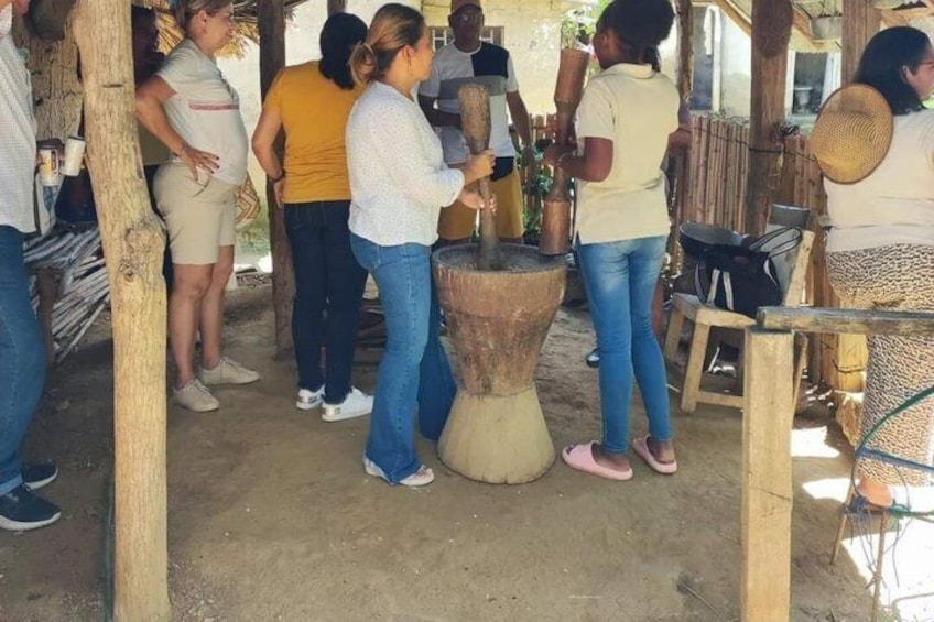 A group of people around a traditional water mill, with a woman operating the mill. 4