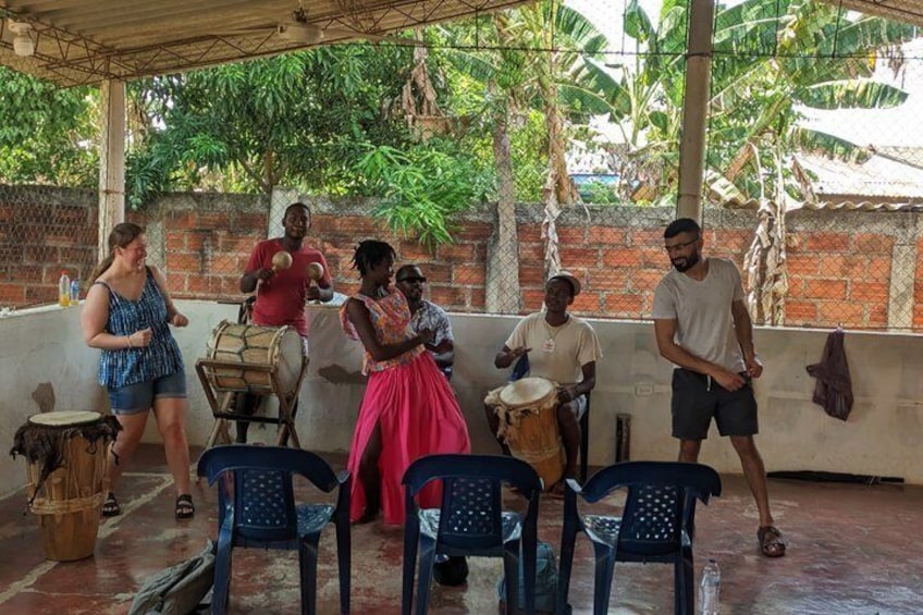 A group of people playing drums in an outdoor setting with chairs and a brick wall in the background. 1