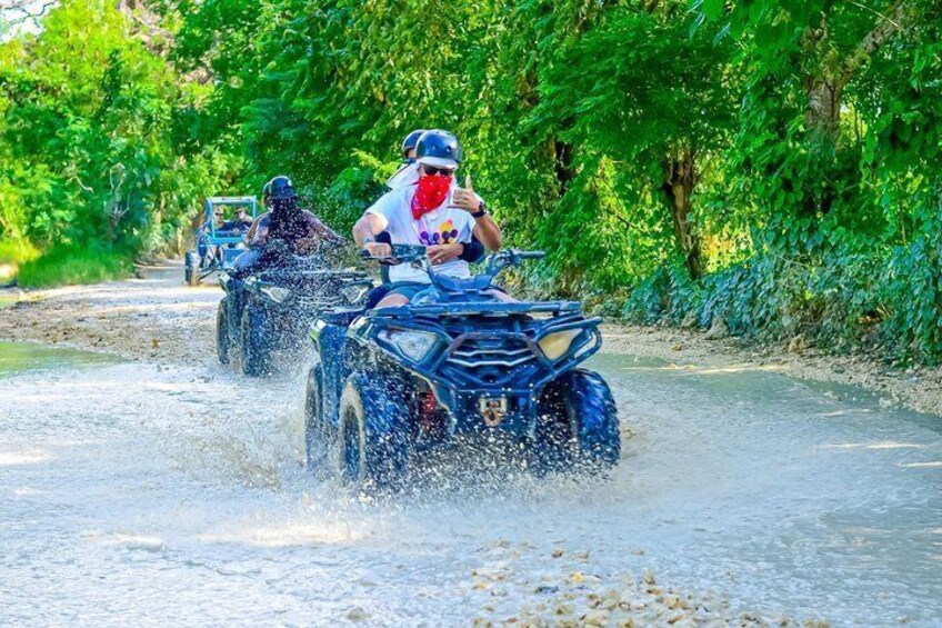 Persone che guidano quad sulla strada allagata, circondate dal verde. 1