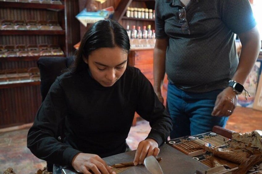 Una persona taglia legno a un tavolo in un laboratorio, sullo sfondo si vedono delle mensole. 4