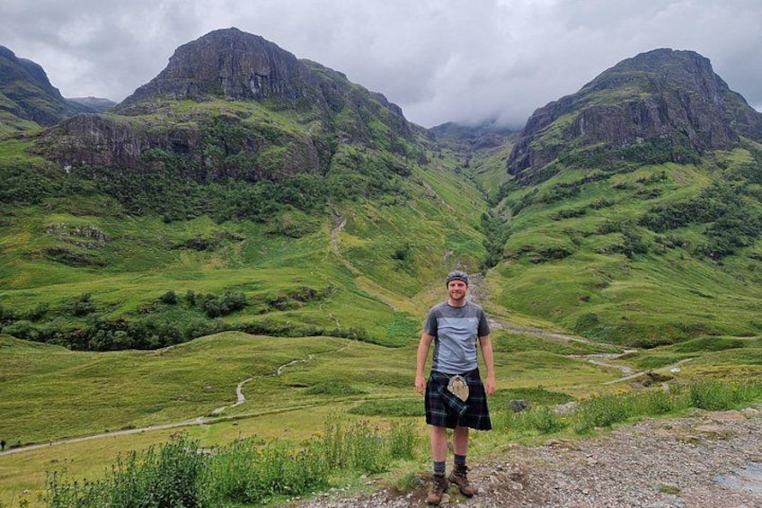 A person standing on a grassy hill with a mountainous landscape in the background. 2