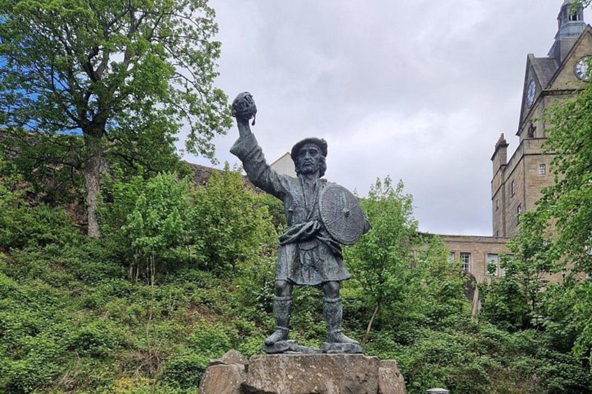 A statue of a historical figure with raised arm, surrounded by greenery and a building in the background. 3