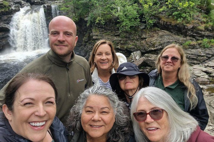 A group of people standing in front of a waterfall with lush greenery in the background. 5