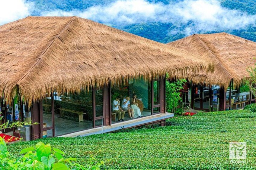 A thatched-roof structure with a glass enclosure, surrounded by lush greenery and mountains in the background. 3