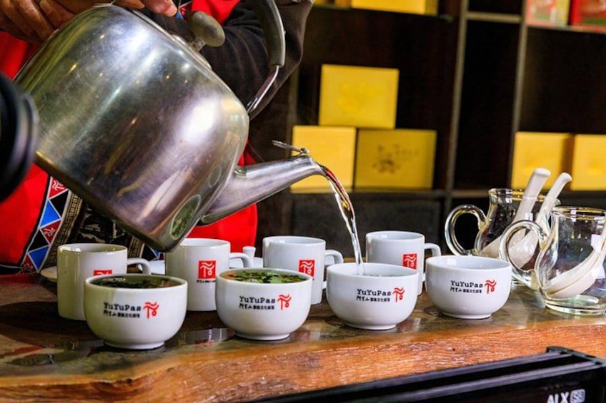 A person pouring tea into white cups with red logos on a wooden table. 3