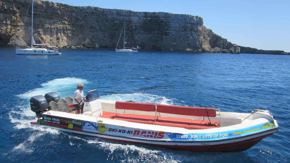 A speedboat with 'OK-KO-KI BANIS' branding on the side, moving through a body of water with cliffs in the background. 3