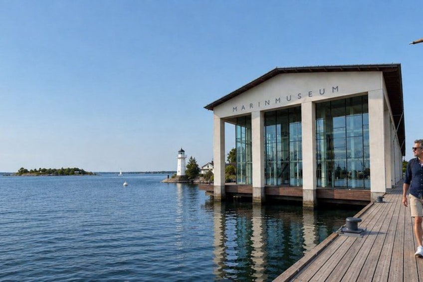 Un hotel marítimo con un muelle de madera que se adentra en una superficie acuática tranquila, un faro al fondo y un cielo despejado. 5
