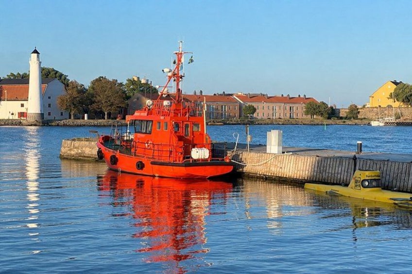 Un bote rojo amarrado en un muelle, con un faro y edificios al fondo. 3