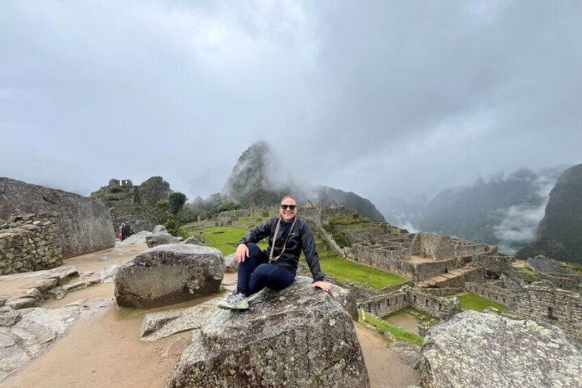 A person sitting on a large rock at Machu Picchu ruins with misty mountains in the background. 2