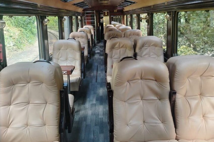 A train interior with beige upholstered seats, wooden tables, and large windows. 5