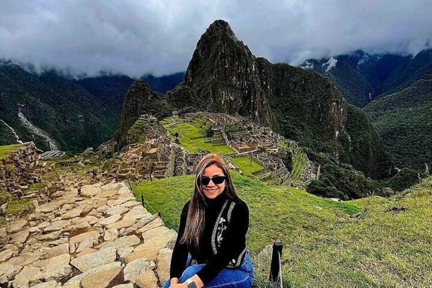 A person sitting on a stone wall with Machu Picchu ruins in the background. 4