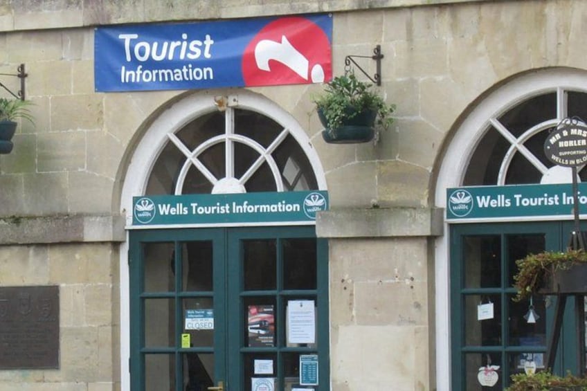 En bygning med to skilte, hvoraf det ene siger 'Wells Tourist Information' og et blåt skilt over dem med teksten 'Tourist Information' og en rød pil, der peger mod højre. 4