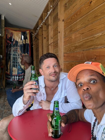 Two people sitting at a red table with green bottles, wooden walls, and a ceiling with a striped pattern. 3