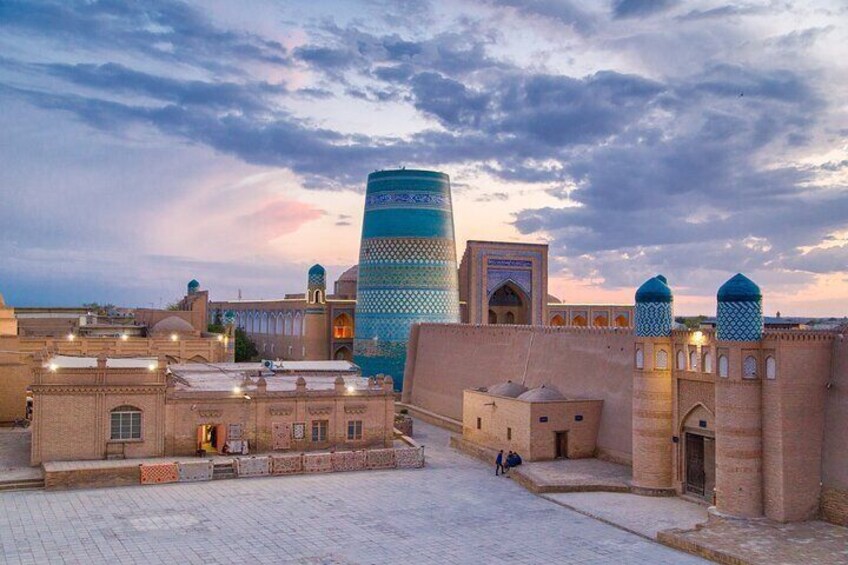 A historic cityscape with traditional architecture, including a prominent minaret and a fortified wall. 1