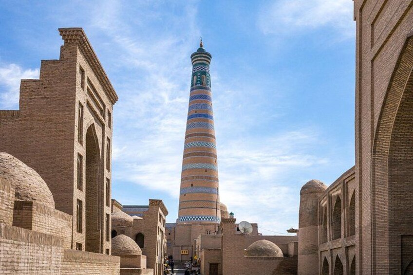 A historic tower with a striped pattern, surrounded by brick buildings and domed structures. 2