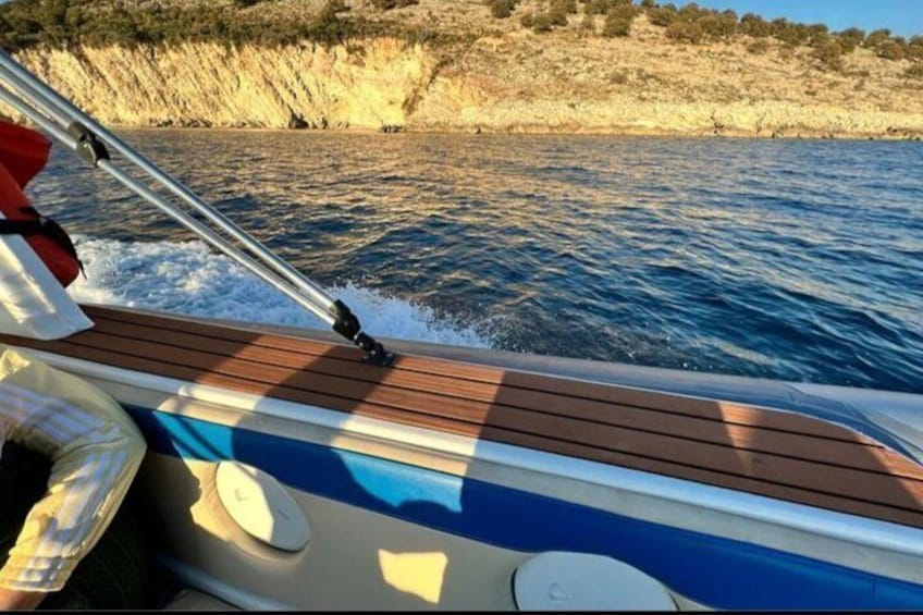 Un bote sobre el agua, con cubierta de madera, timón y una costa rocosa al fondo. 3
