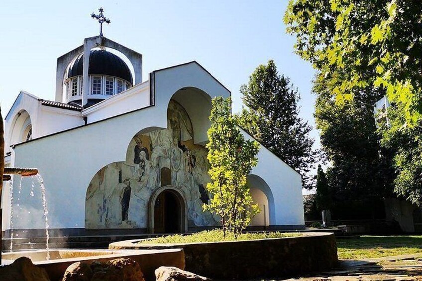 Una iglesia con cúpula y ventanas de arco, rodeada de árboles y una fuente. 4