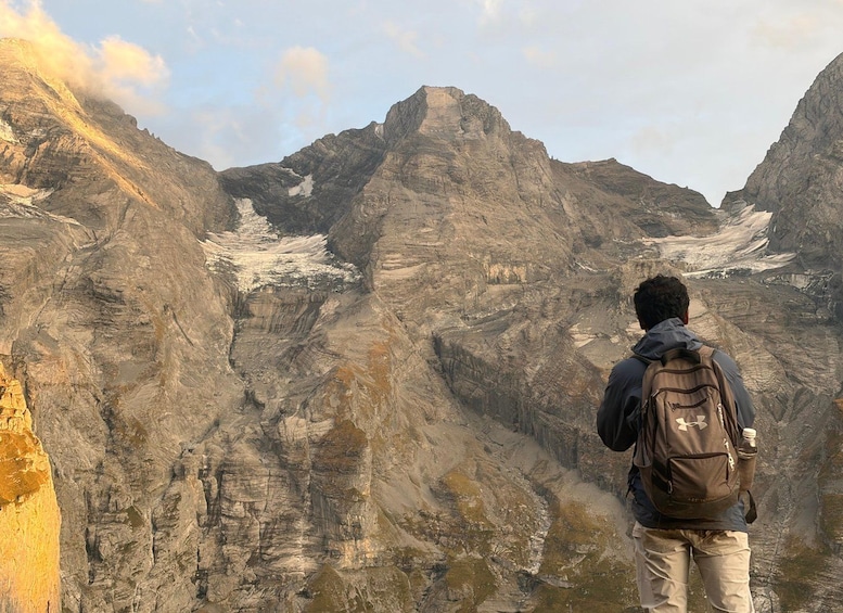 A person standing on a mountain ridge, overlooking a valley with exposed rock faces and patches of snow. 5