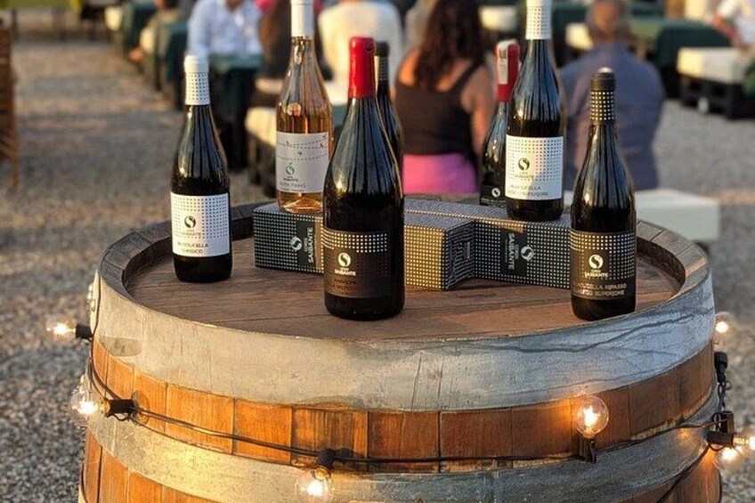 A wooden barrel with wine bottles on top, surrounded by string lights. 3