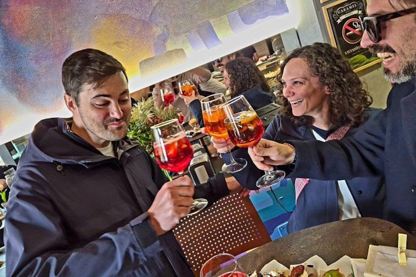 People toasting with drinks at a bar with a colorful mural in the background. 2