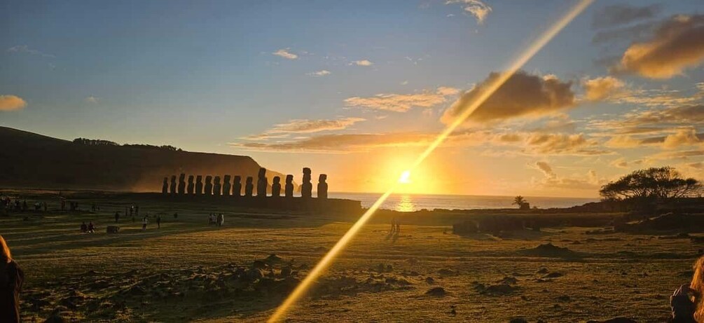A sunset over a field with a row of statues, a clear sky, and distant hills. 5