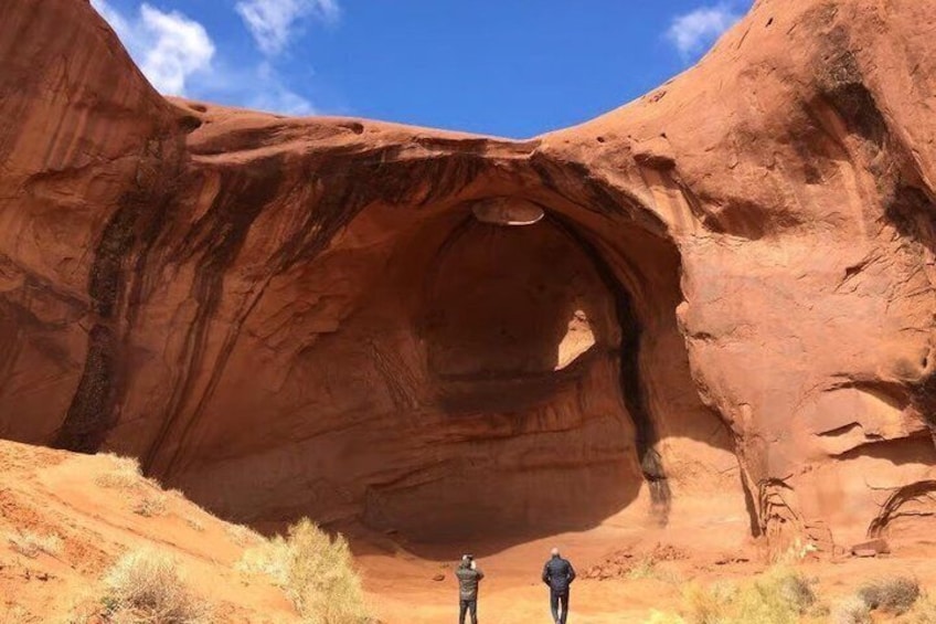 Une grande formation rocheuse rouge, dotée d’une arche naturelle, devant laquelle se tiennent deux personnes. 5
