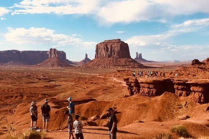A desert landscape with rock formations and a group of people standing on a ridge. 2