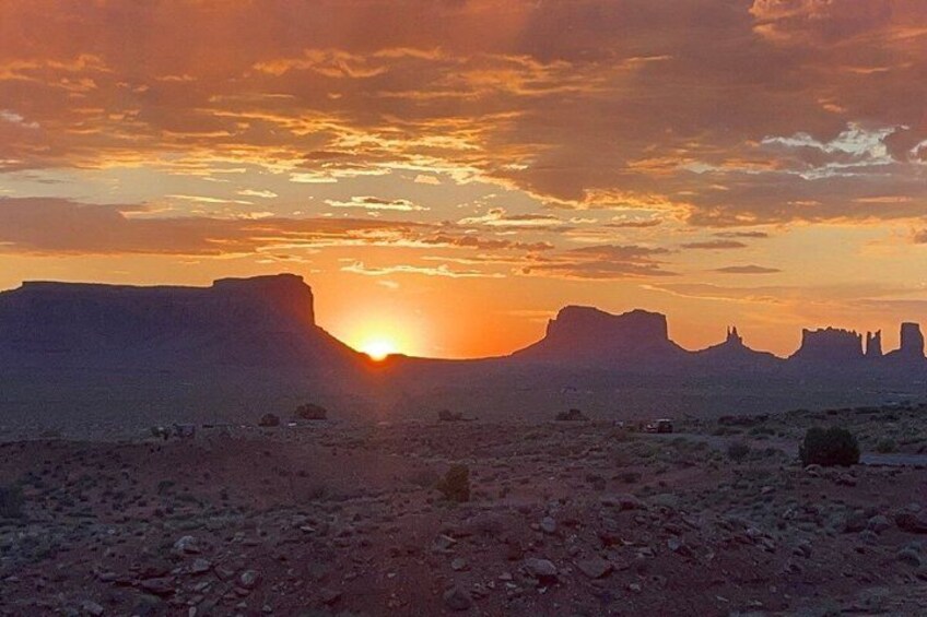 A desert landscape with a sunset, rock formations, and sparse vegetation. 4