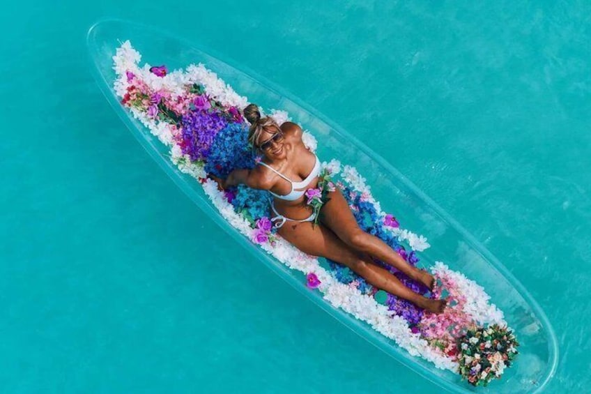A person lying on a floating platform in a clear blue pool, surrounded by colorful flowers. 1