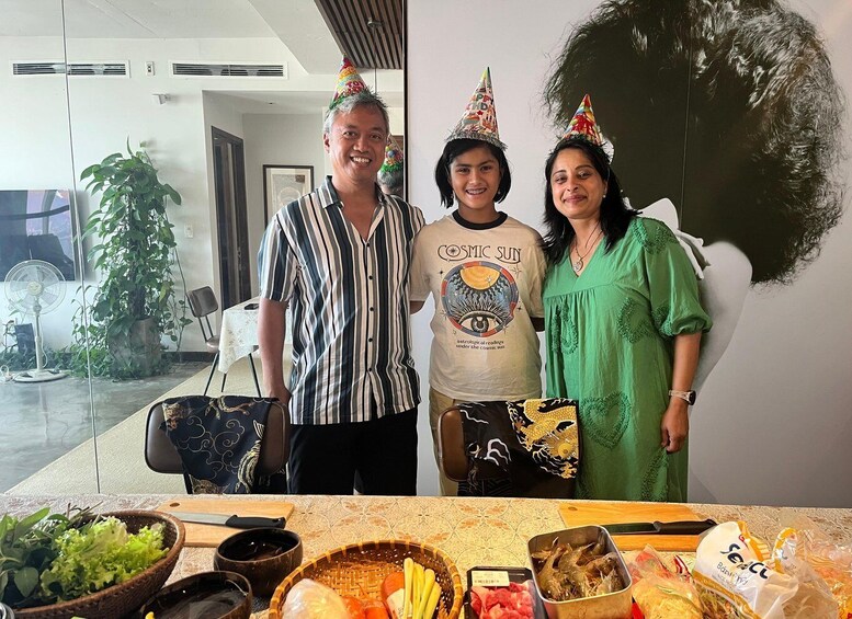 Three people standing in a room with a table of food items in front of them. 2