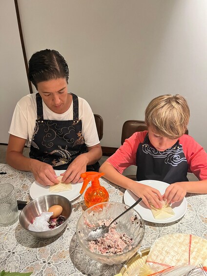 Two people preparing food at a table with a lace tablecloth, a metal bowl, and a plastic bag. 3