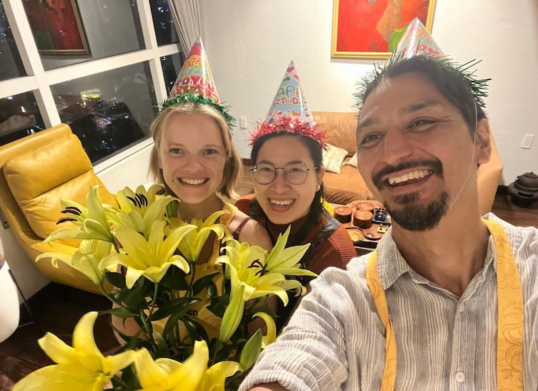 Three people wearing party hats, a yellow chair, and a potted plant with yellow flowers. 1
