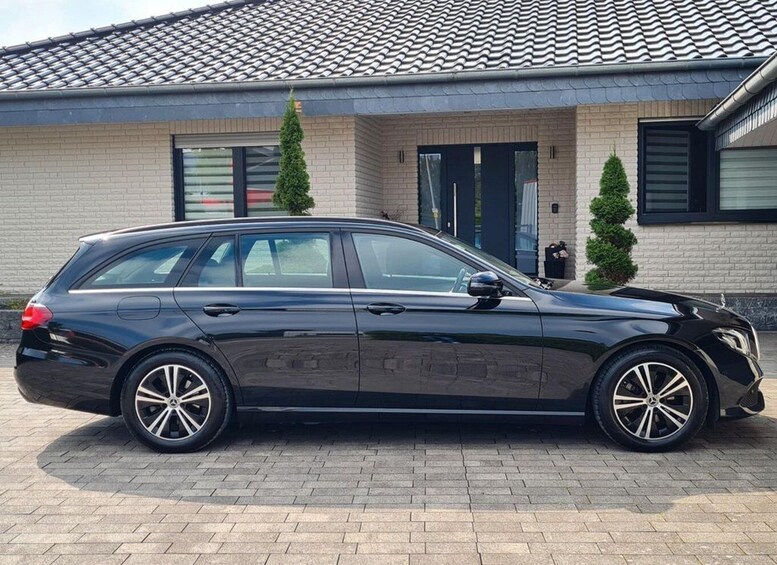A black station wagon parked in front of a house with a tiled roof and brick walls. 5