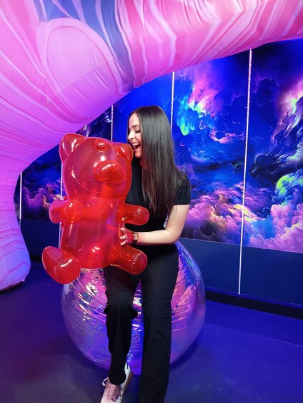 A person holding a red bear-shaped balloon in front of a colorful, abstract mural. 4