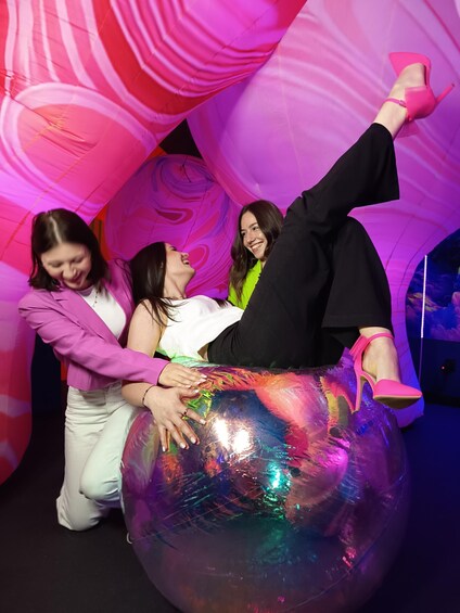 Three people sitting on a large, reflective ball with a colorful, swirling background. 1