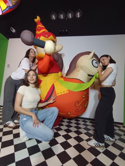 A group of people posing with a large inflatable character in a room with a checkered floor and a green wall. 2
