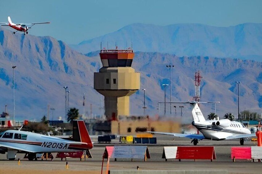 Un aeropuerto con varios aviones, una torre de control y montañas al fondo. 4