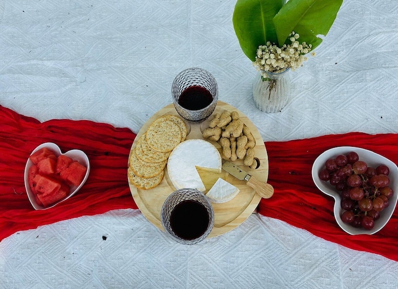 A cheese platter with crackers, grapes, and a heart-shaped watermelon on a red cloth. 3