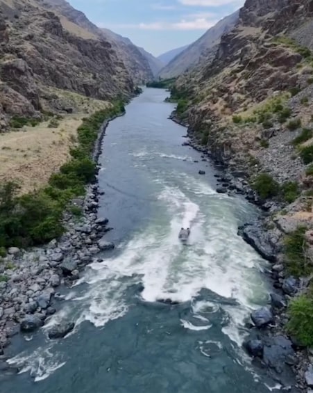 A river flowing through a canyon with rocky banks and a boat navigating the rapids. 2
