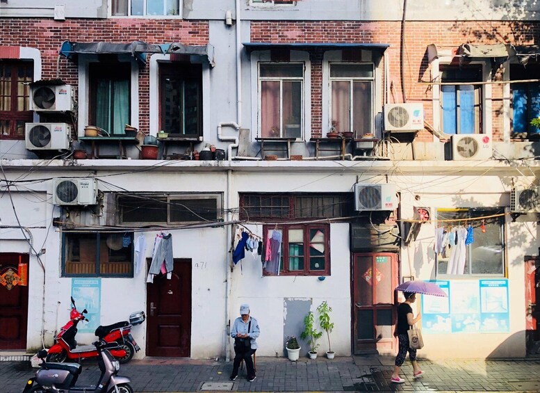 A multi-story residential building with laundry hanging outside, a parked scooter, and a person walking with an umbrella. 3