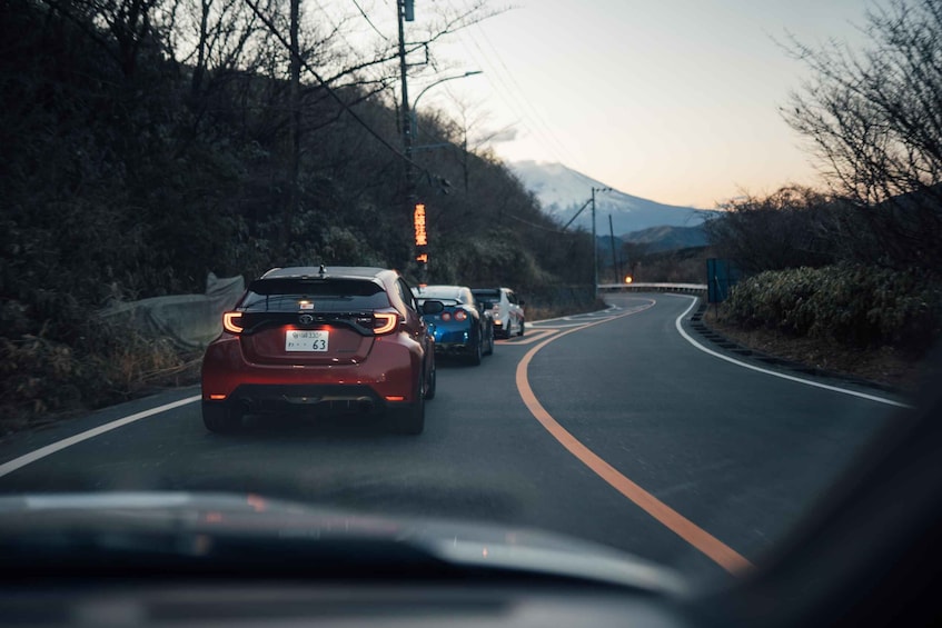 A winding road with vehicles, surrounded by trees and a mountain in the background. 3