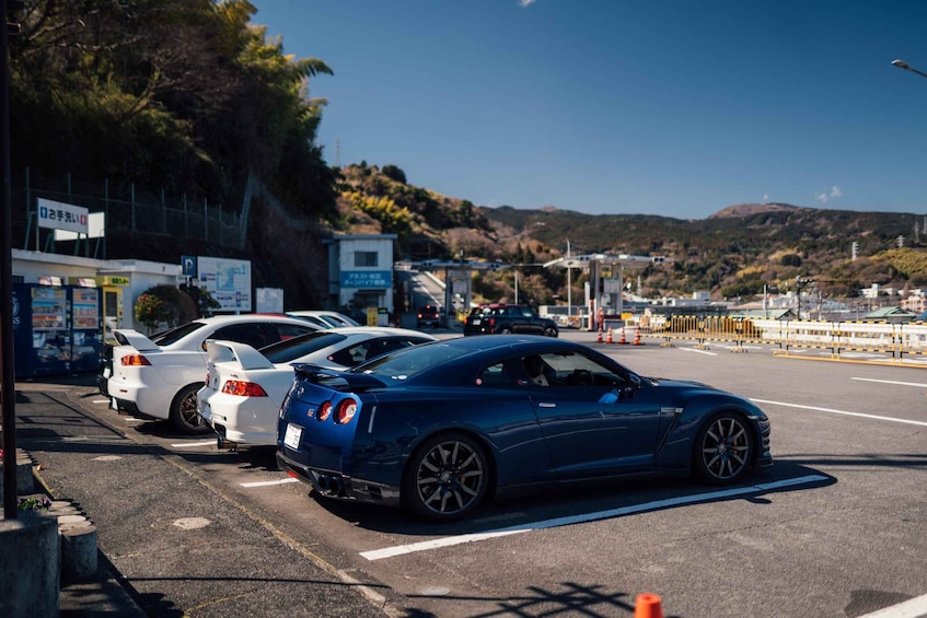 A parking lot with several sports cars, a building with signage, and a hilly landscape in the background. 4