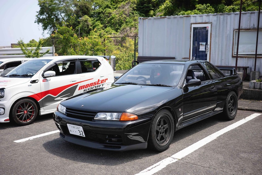 A black sports car parked in a lot with a white and red vehicle behind it. 2