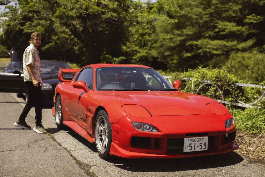 A red sports car parked on a paved road with a person walking behind it. 5