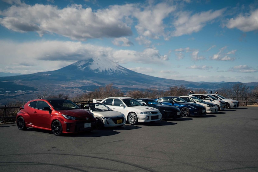 A row of sports cars parked in a lot with a mountain in the background. 1