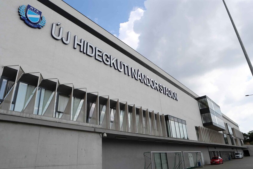 A building with a sign reading 'ÚJ HIDEGKUTI NÁNDORSTÁJON' and a logo with 'MTK' and the year '1880'. 4
