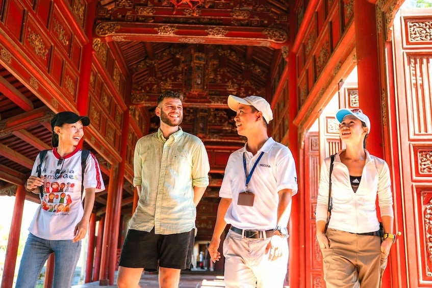 A group of people walking through a red-roofed corridor with ornate carvings. 1