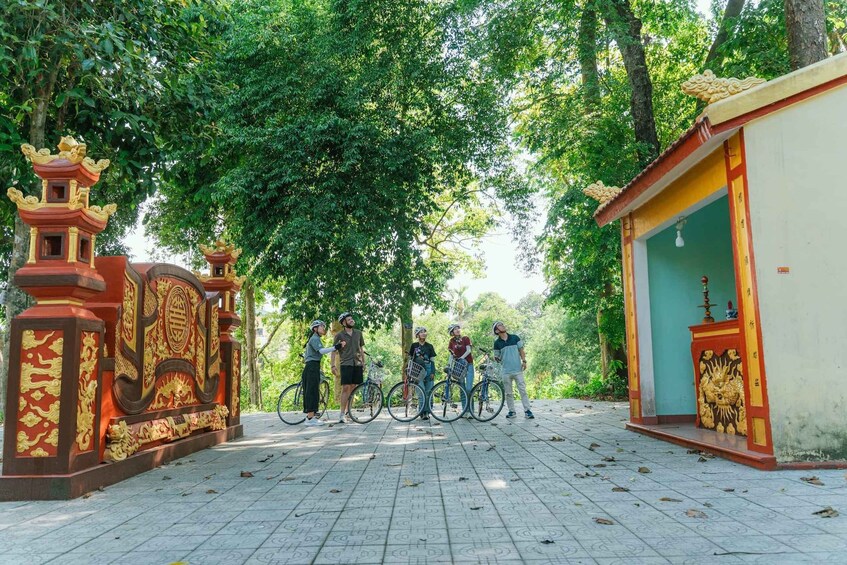 A group of people with bicycles near a traditional gate with ornate designs, surrounded by lush greenery. 2