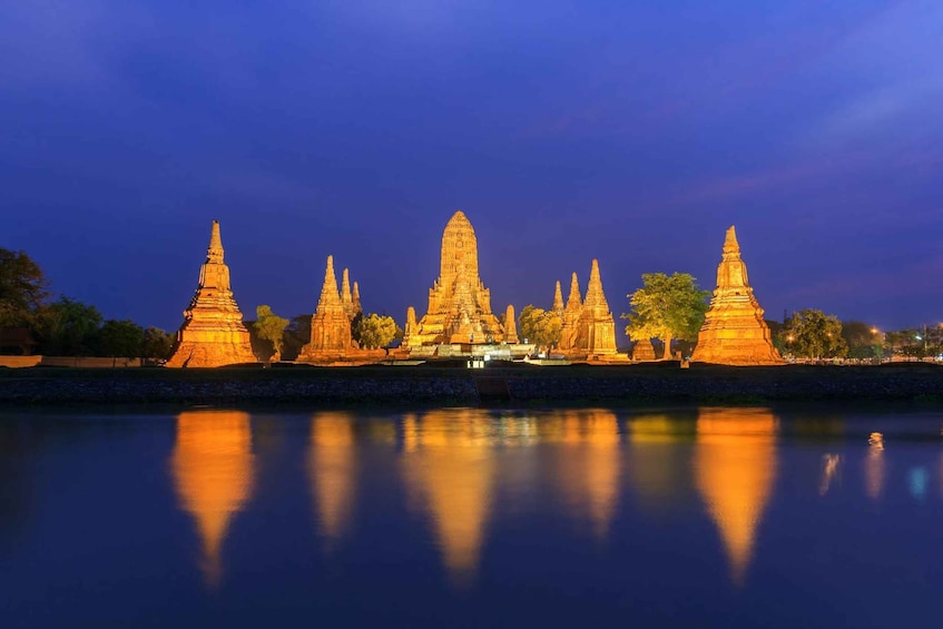 A series of illuminated temple structures by a calm river at dusk. 3